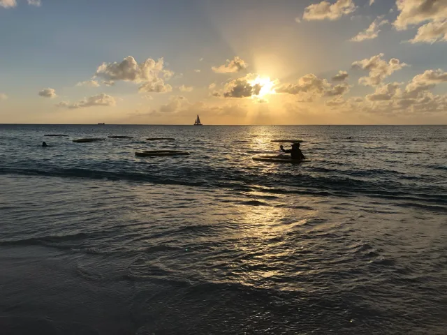 グランドケイマンの海。水平線の上に太陽と雲があり、手前に小舟が浮かぶ