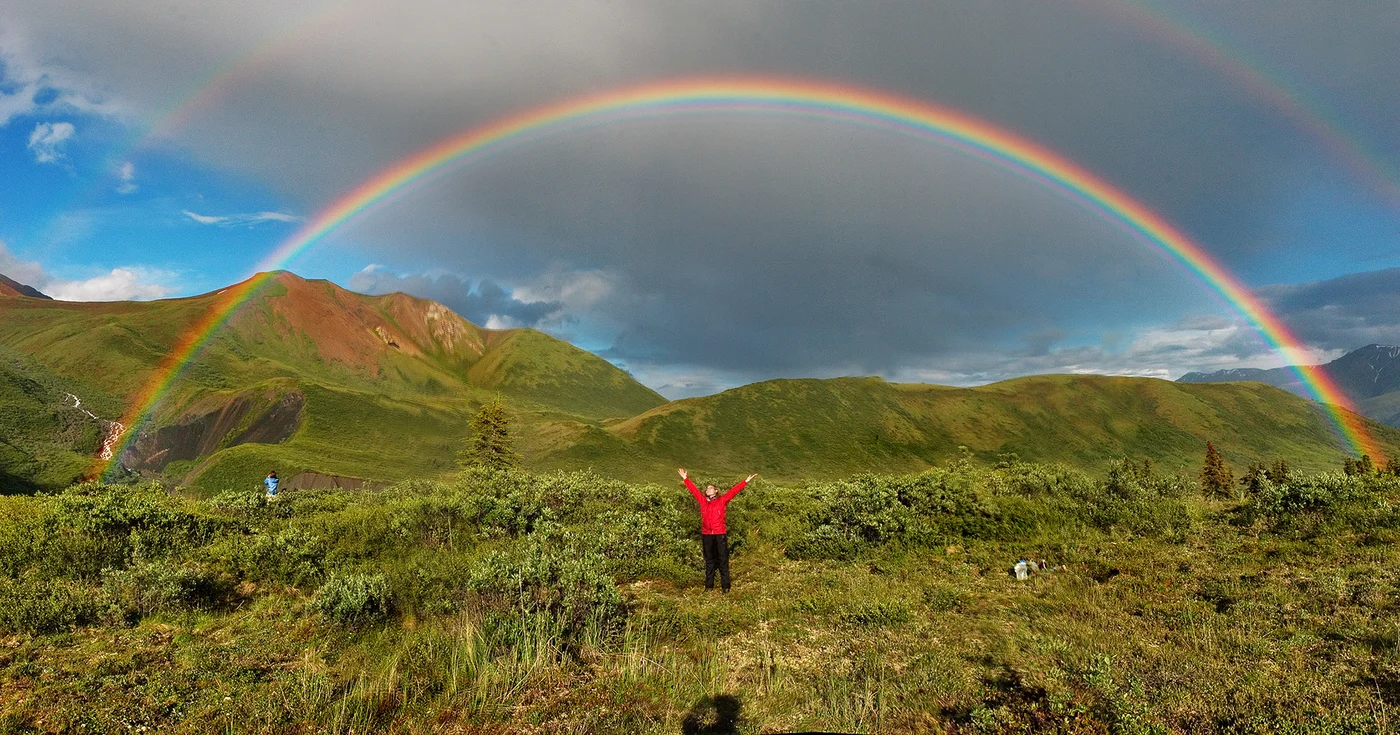 アラスカの山並みにかかる明るい虹と、その外側の左右に見える薄い虹